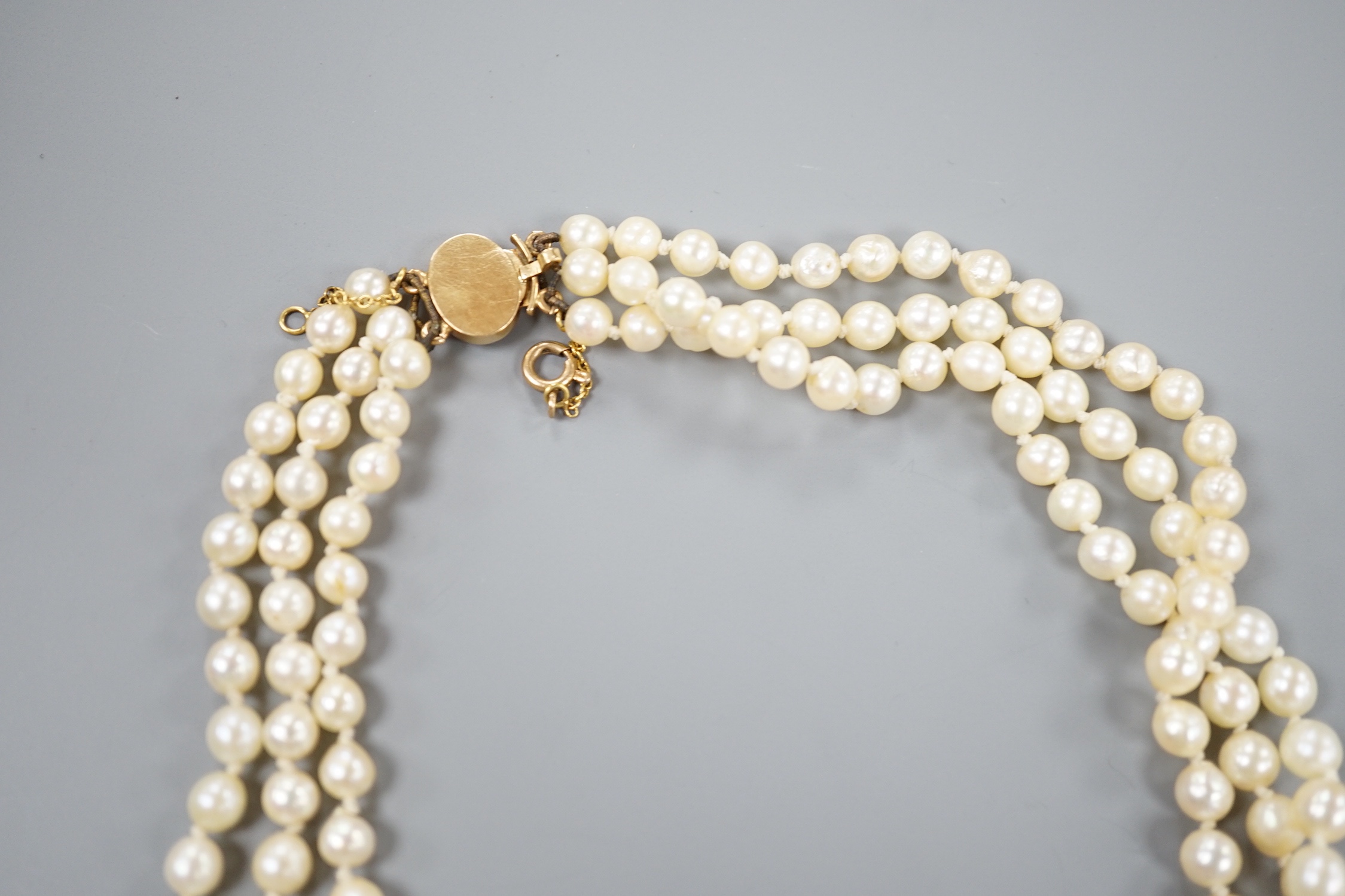 A triple strand graduated cultured pearl necklace, with yellow metal clasp, 50cm.